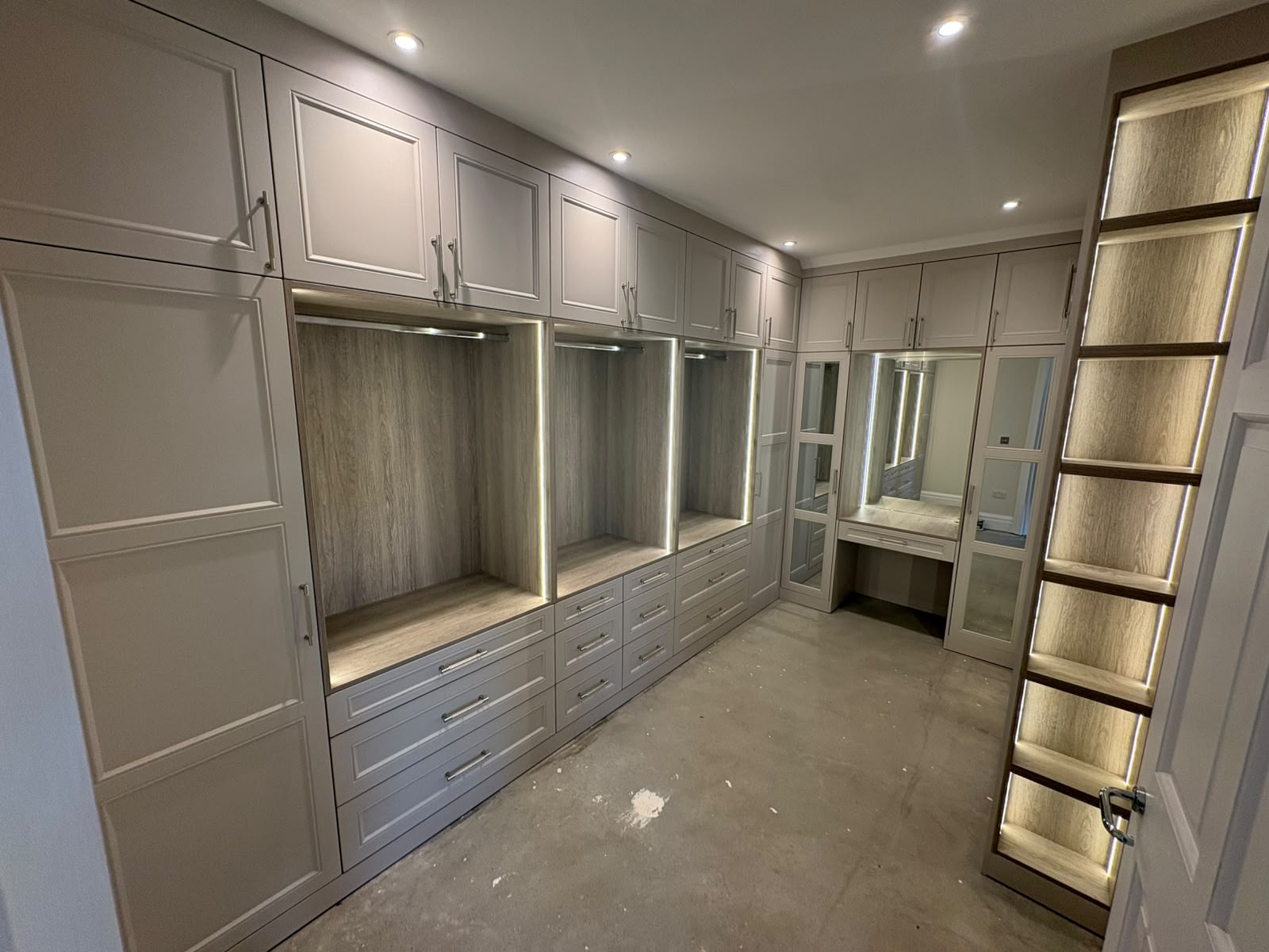 Grey bespoke walk-in wardrobe with illuminated hanging bays, drawers and vanity